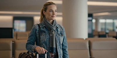 White female travel nurse with a carry-on bag in an airport lounge